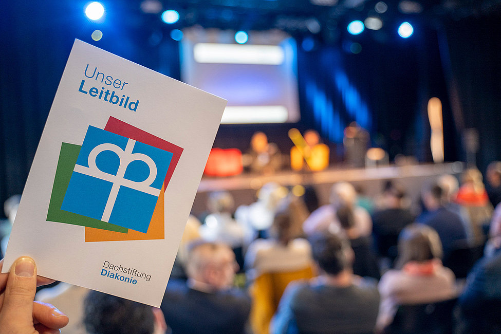 Hand hält Broschüre Unser Leitbild Dachstiftung Diakonie vor Veranstaltung
