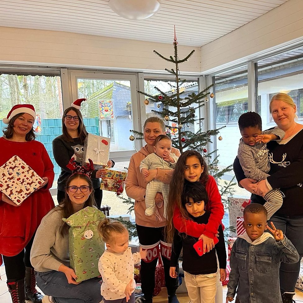 VW-Mitarbeitende und Kinder mit Geschenken vor geschmücktem Weihnachtsbaum in Flüchtlingsunterkunft