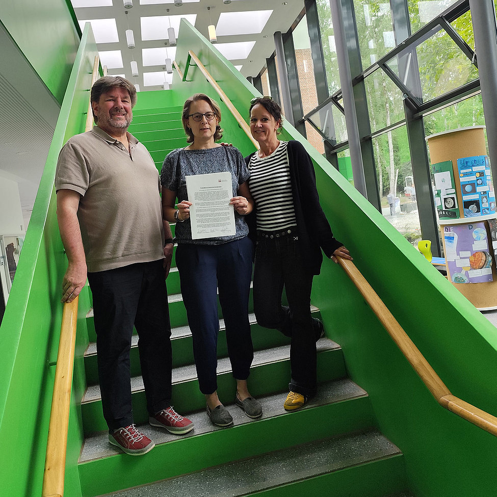Drei Personen auf grüner Treppe halten Kooperationsvereinbarung