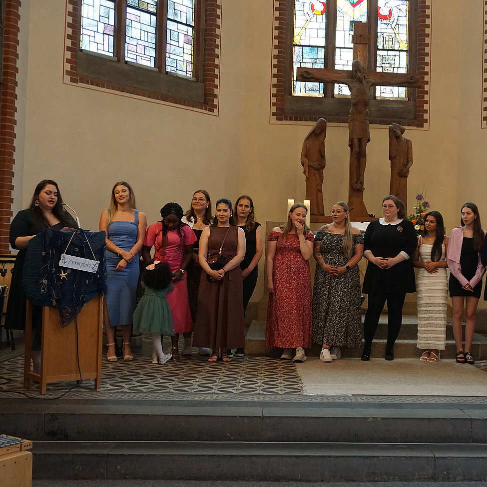 Abschlussgruppe in Kirche vor Kreuz, Rednerin am Pult Ankerplatz